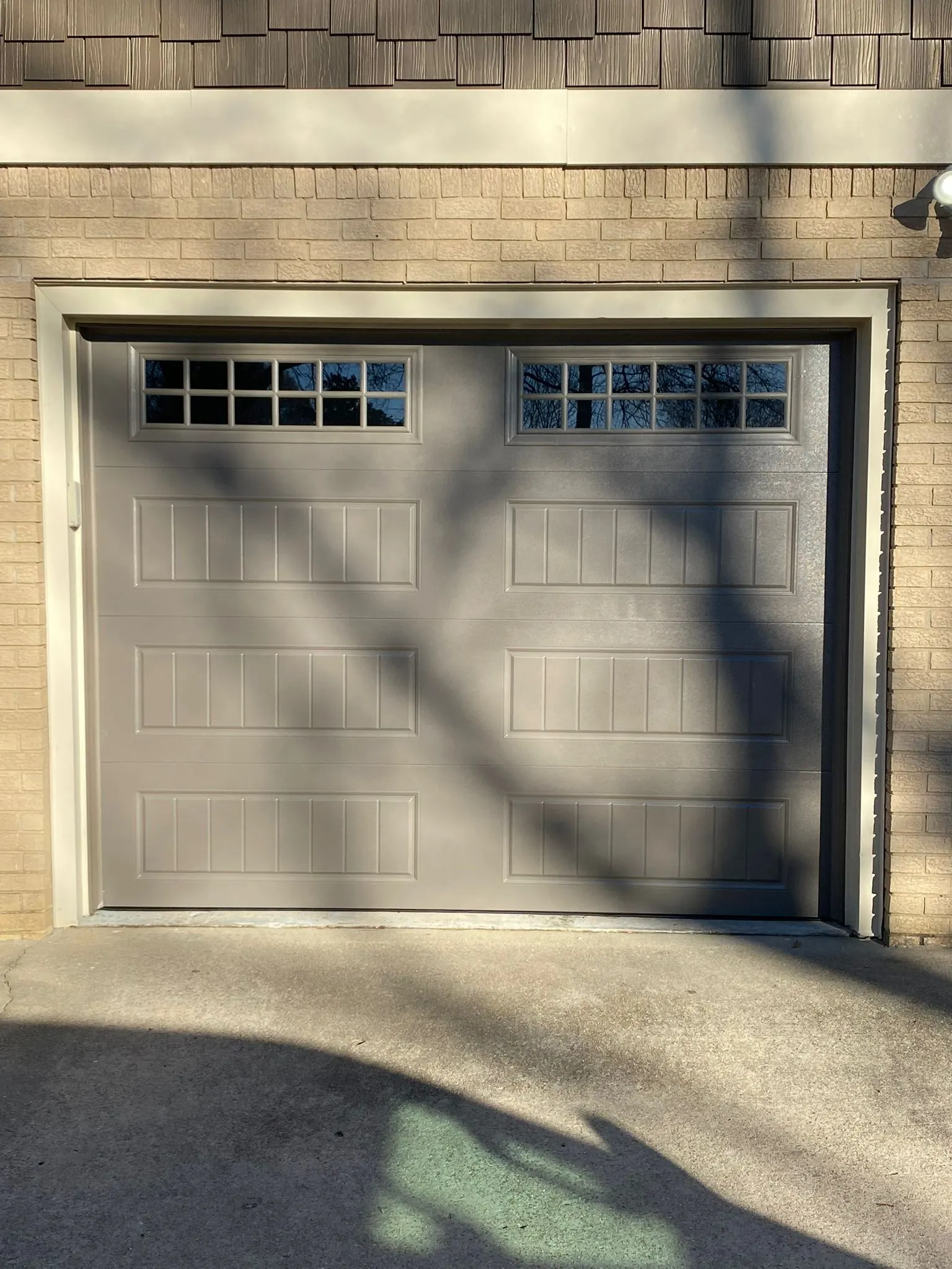 Single-car raised-panel garage door with window inserts on a brick home